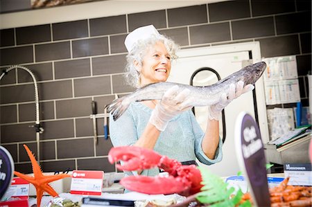 simsearch:649-08923766,k - Supermarket worker behind counter, holding fresh fish, smiling Foto de stock - Royalty Free Premium, Número: 649-08923776