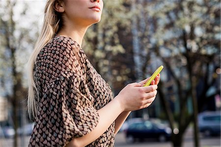simsearch:649-07280834,k - Cropped shot of young woman with smartphone looking over her shoulder in city Stock Photo - Premium Royalty-Free, Code: 649-08923910