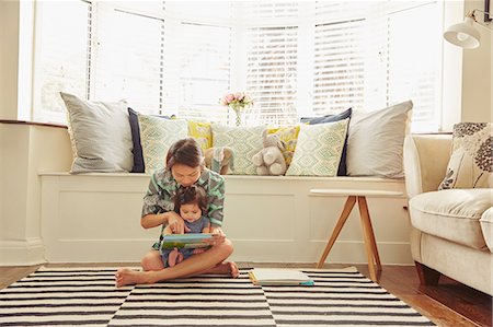 dressing - Baby girl sitting on mother's lap reading book in living room Stock Photo - Premium Royalty-Free, Code: 649-08949444