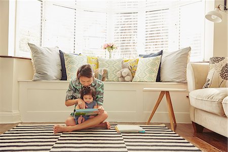 simsearch:649-08661494,k - Baby girl sitting on mother's lap reading book in living room Fotografie stock - Premium Royalty-Free, Codice: 649-08949444