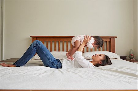 simsearch:649-08661489,k - Woman lying on bed holding up baby daughter Foto de stock - Royalty Free Premium, Número: 649-08949478