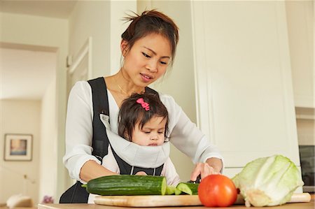 simsearch:649-08661494,k - Woman with baby daughter in sling slicing salad at kitchen counter Fotografie stock - Premium Royalty-Free, Codice: 649-08949472