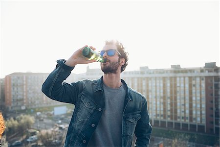 simsearch:649-08949691,k - Young man drinking from beer bottle at roof party Photographie de stock - Premium Libres de Droits, Code: 649-08949669