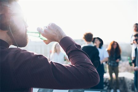simsearch:649-08949687,k - Group of friends enjoying roof party, young man drinking from beer bottle Stock Photo - Premium Royalty-Free, Code: 649-08949674