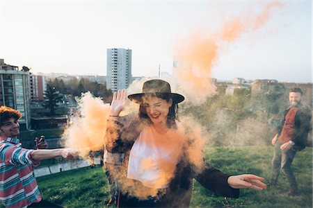 simsearch:649-08949675,k - Group of friends on roof, holding colourful smoke flares, young woman walking through orange smoke Foto de stock - Sin royalties Premium, Código: 649-08949690