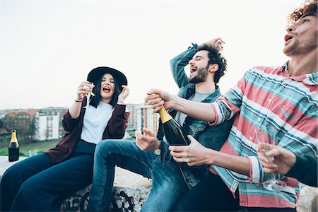 Group of friends enjoying roof party, young man opening bottle of champagne Stock Photo - Premium Royalty-Free, Code: 649-08949705