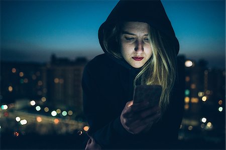 sentimiento de soledad - Young woman sitting on rooftop at night, using smartphone, illuminating face Foto de stock - Sin royalties Premium, Código: 649-08949717