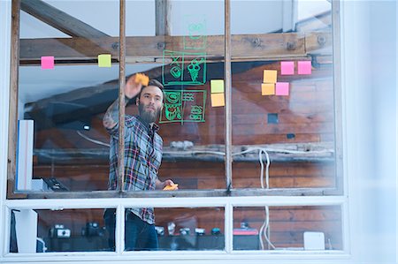 sacar fotos - Young male designer removing adhesive note from design studio window Photographie de stock - Premium Libres de Droits, Code: 649-08949822