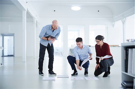 Colleagues working in open plan office looking at blueprints Stock Photo - Premium Royalty-Free, Code: 649-08950486