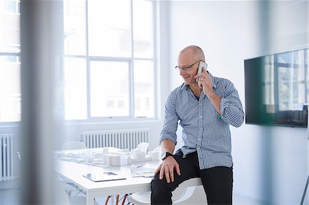 Man sitting on desk in office making telephone call on mobile phone Stock Photo - Premium Royalty-Free, Code: 649-08950480