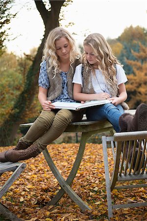 simsearch:649-08950750,k - Portrait of two sisters sitting on patio table reading book in autumn garden Stock Photo - Premium Royalty-Free, Code: 649-08950735
