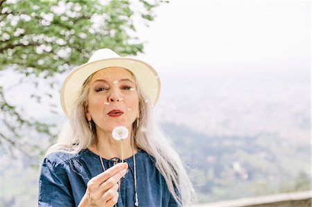 Mature woman with long grey hair blowing dandelion clock, Fiesole, Tuscany, Italy Fotografie stock - Premium Royalty-Free, Codice: 649-08951140