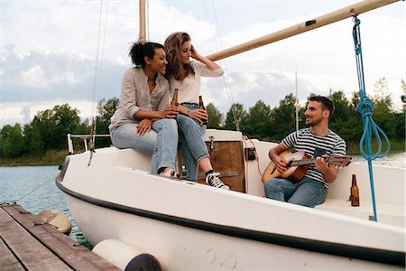 sailing music - Three friends relaxing on moored sailing boat, drinking beer, man playing guitar Stock Photo - Premium Royalty-Free, Code: 649-08969347