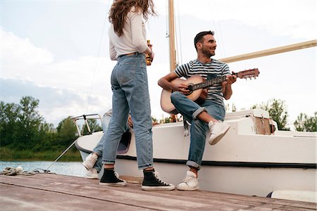 sailing music - Three friends relaxing on pier, sitting on sailing boat, man playing guitar Stock Photo - Premium Royalty-Free, Code: 649-08969349