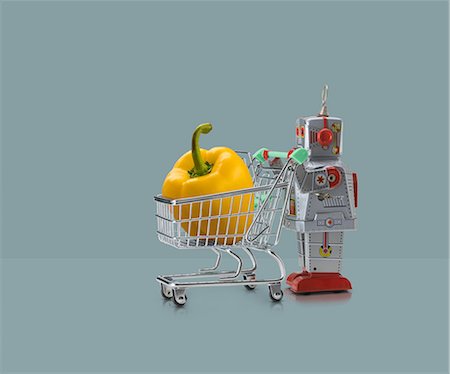 simsearch:649-08423033,k - Toy robot pushing miniature shopping trolley with yellow pepper against blue background Stock Photo - Premium Royalty-Free, Code: 649-08969534