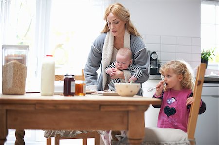 desayuno - Mother holding baby boy, sitting at kitchen table with young daughter, having breakfast Foto de stock - Sin royalties Premium, Código: 649-08969814
