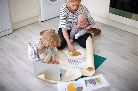 Woman holding baby son in arms, looking through graphs on kitchen floor, young daughter holding paper open Photographie de stock - Premium Libres de Droits, Code: 649-08969826