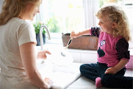 simsearch:649-08576682,k - Mother and daughter in kitchen, daughter sitting on work surface helping mother with washing up Fotografie stock - Premium Royalty-Free, Codice: 649-08969822