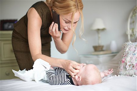 Mother changing baby son's nappy while using mobile phone Foto de stock - Sin royalties Premium, Código: 649-08969864