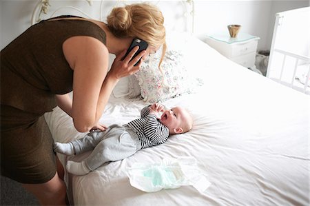 Mother changing baby son's nappy while using mobile phone Foto de stock - Sin royalties Premium, Código: 649-08969863