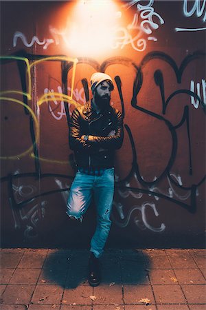 dim illumination photo - Portrait of cool young male hipster leaning against graffiti wall at night Stock Photo - Premium Royalty-Free, Code: 649-08969980