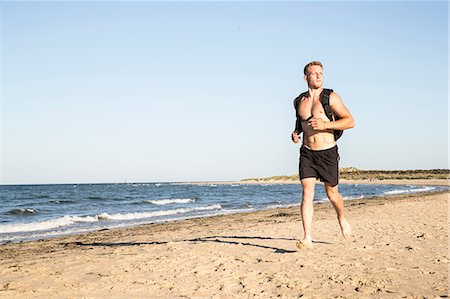 simsearch:649-08702370,k - Young male runner wearing shorts and backpack running along beach Stock Photo - Premium Royalty-Free, Code: 649-08988270