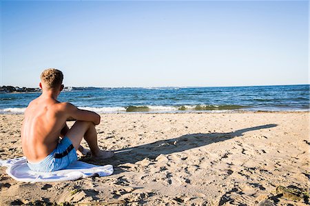 simsearch:6128-08798873,k - Young man sitting on beach looking out to sea Foto de stock - Sin royalties Premium, Código: 649-08988273