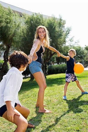 family child vacation italy - Kids pulling young woman's hand on lawn Stock Photo - Premium Royalty-Free, Code: 649-09002278