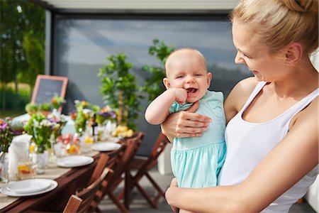 simsearch:614-06897874,k - Young woman carrying baby daughter at family lunch by patio table Photographie de stock - Premium Libres de Droits, Code: 649-09025499