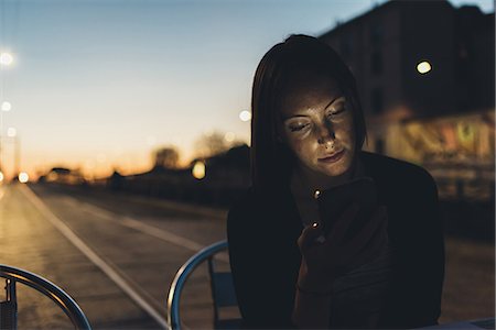 front of face looking down - Young woman on street looking at smartphone at dusk Stock Photo - Premium Royalty-Free, Code: 649-09025526