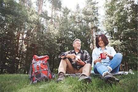 simsearch:649-08381585,k - Mature couple relaxing on grass, holding tin cups, rucksack beside them Stock Photo - Premium Royalty-Free, Code: 649-09025685