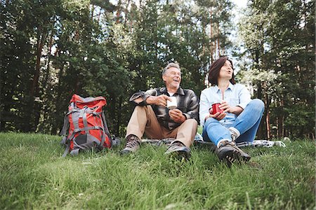 simsearch:649-08381585,k - Mature couple relaxing on grass, holding tin cups, rucksack beside them Stock Photo - Premium Royalty-Free, Code: 649-09025682