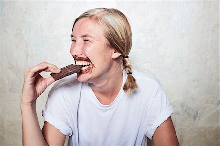 simsearch:614-06168625,k - Woman eating bar of chocolate, chocolate around mouth, laughing Stock Photo - Premium Royalty-Free, Code: 649-09025836