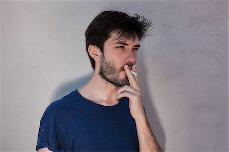 simsearch:649-08060336,k - Young man with beard smoking cigarette in front of cement wall Stock Photo - Premium Royalty-Free, Code: 649-09026187