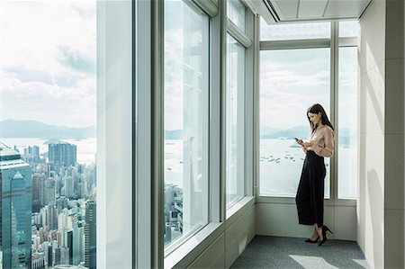 simsearch:649-09035446,k - Business woman in skyscraper office window using smartphone Photographie de stock - Premium Libres de Droits, Code: 649-09035447