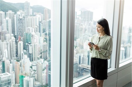 Businesswoman with smartphone looking out of window Stock Photo - Premium Royalty-Free, Code: 649-09035458