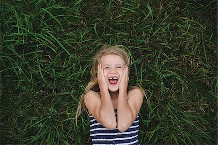 Overhead portrait of girl lying on grass with hands on her cheeks Fotografie stock - Premium Royalty-Free, Codice: 649-09035544