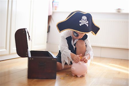 Young boy dressed as pirate, putting money into piggy bank Stock Photo - Premium Royalty-Free, Code: 649-09035553