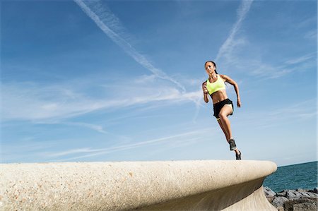 simsearch:649-08988270,k - Low angle view of young female runner running along sea wall against blue sky Foto de stock - Sin royalties Premium, Código: 649-09035644