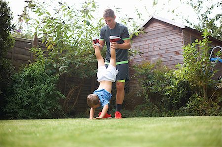 father teaching his child - Father and son in garden, son's hands on grass, father lifting his legs Foto de stock - Sin royalties Premium, Código: 649-09035787