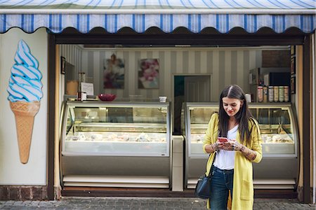 Young woman, outside ice cream parlour, using smartphone Stock Photo - Premium Royalty-Free, Code: 649-09036141