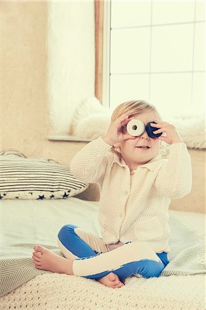 simsearch:614-06974043,k - Female toddler sitting on bed peeking through circles covering eyes Foto de stock - Sin royalties Premium, Código: 649-09036174