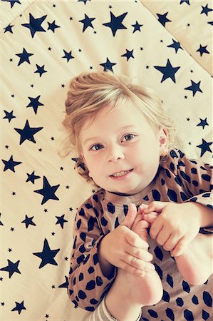 simsearch:649-06488477,k - Portrait of female toddler lying on star pattern bed holding her bare feet Photographie de stock - Premium Libres de Droits, Code: 649-09036180