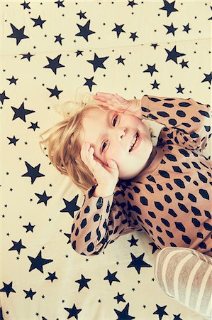 Portrait of female toddler lying on star pattern bed with hands on cheeks Stock Photo - Premium Royalty-Free, Code: 649-09036183