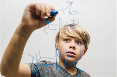 Close up of boy's hand writing equation onto glass wall Stock Photo - Premium Royalty-Free, Code: 649-09036355