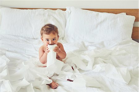 Toddler sitting on bed, holding unravelled toilet roll Stock Photo - Premium Royalty-Free, Code: 649-09036402