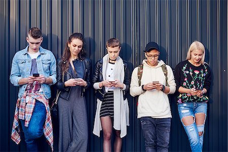 simsearch:649-09061458,k - Row of five young adult friends leaning against black wall looking at smartphones Stock Photo - Premium Royalty-Free, Code: 649-09061244