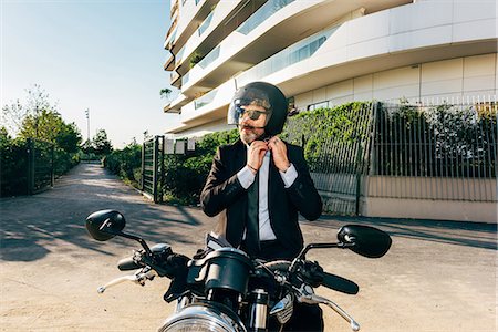 Mature businessman outdoors, sitting on motorcycle, putting on motorcycle helmet Stock Photo - Premium Royalty-Free, Code: 649-09061334