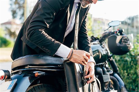 Mature businessman outdoors, leaning over motorcycle, doing up bag, mid section Stock Photo - Premium Royalty-Free, Code: 649-09061337