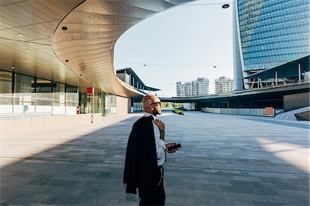 Mature businessman walking outdoors, carrying suit jacket over shoulder, holding smartphone Stock Photo - Premium Royalty-Free, Code: 649-09061331